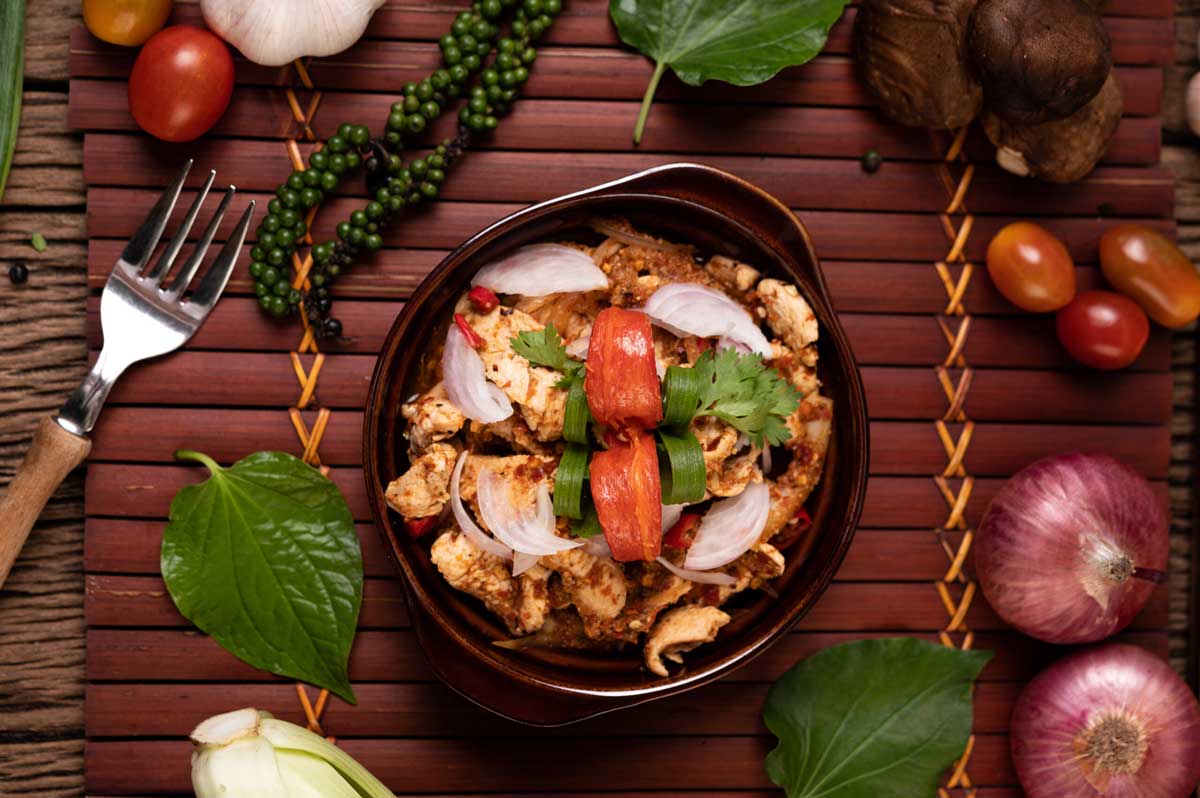 A delicious bowl of spiced chicken topped with tomatoes, onions, and herbs, surrounded by fresh vegetables and a fork.